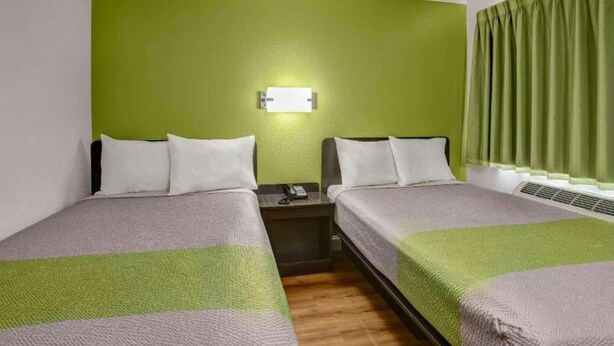 Habitación de hotel con dos camas, una mesita de noche, un teléfono y una lámpara fijada a la pared.