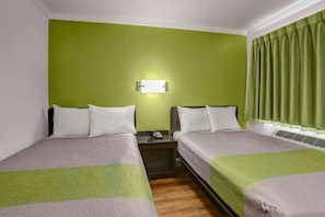 A hotel room with two beds, a nightstand, a telephone, and a wall-mounted light fixture.