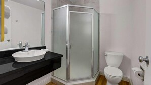 Un baño con ducha envuelta en vidrio, inodoro blanco y encimera negra con lavamanos blanco.