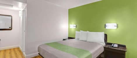 A hotel room with a bed, bedside table, and a green accent wall.