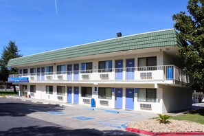 Un motel con techo verde, varias habitaciones y estacionamiento.