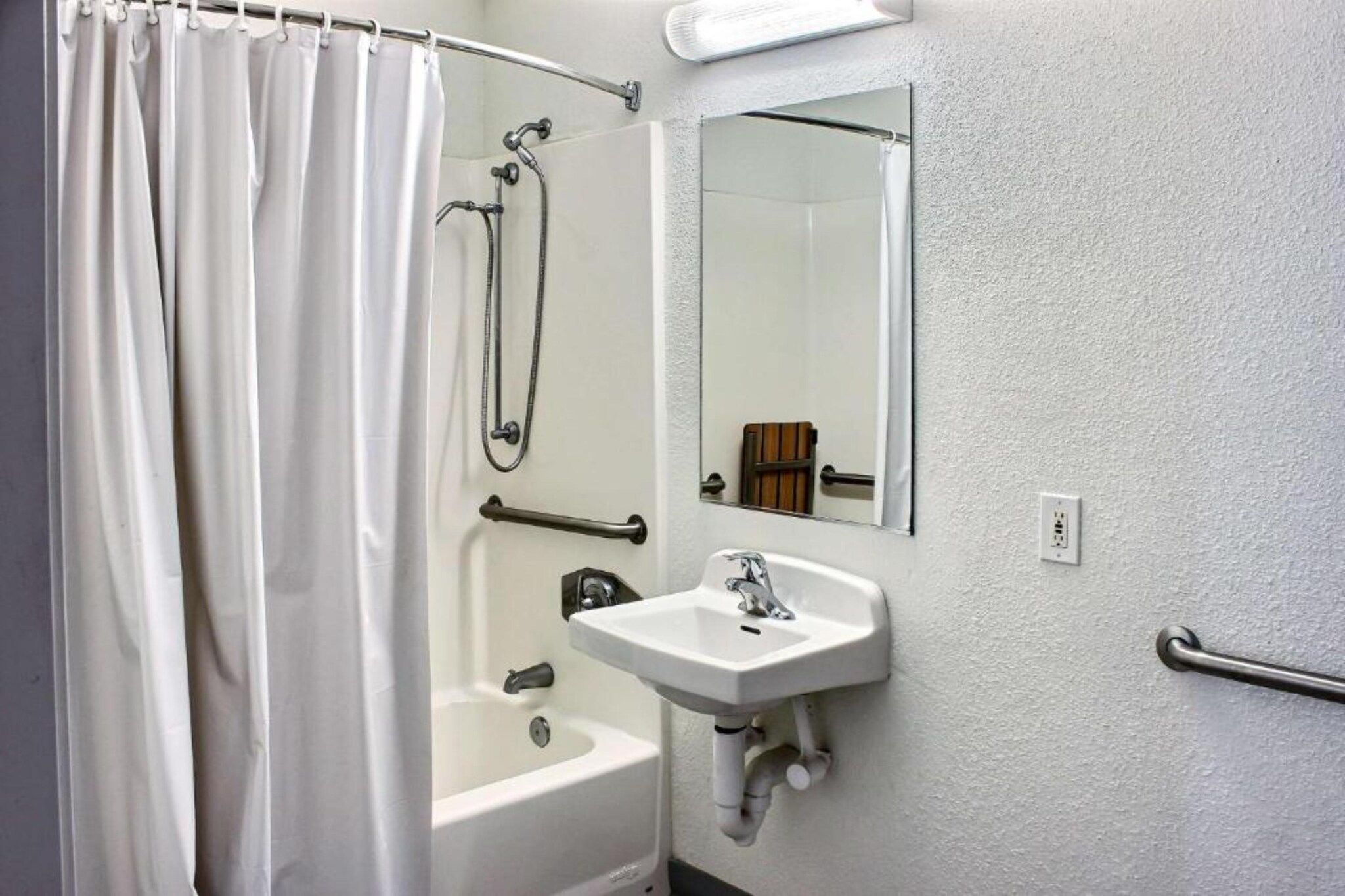 Een badkamer met douchegordijn, bad, wastafel en spiegel.