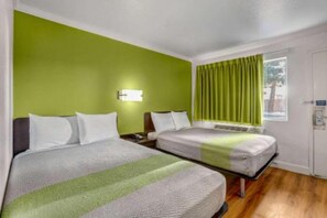 Una habitación de hotel con dos camas, una pared verde, un ventanal con cortinas y una mesita de noche con lámpara.