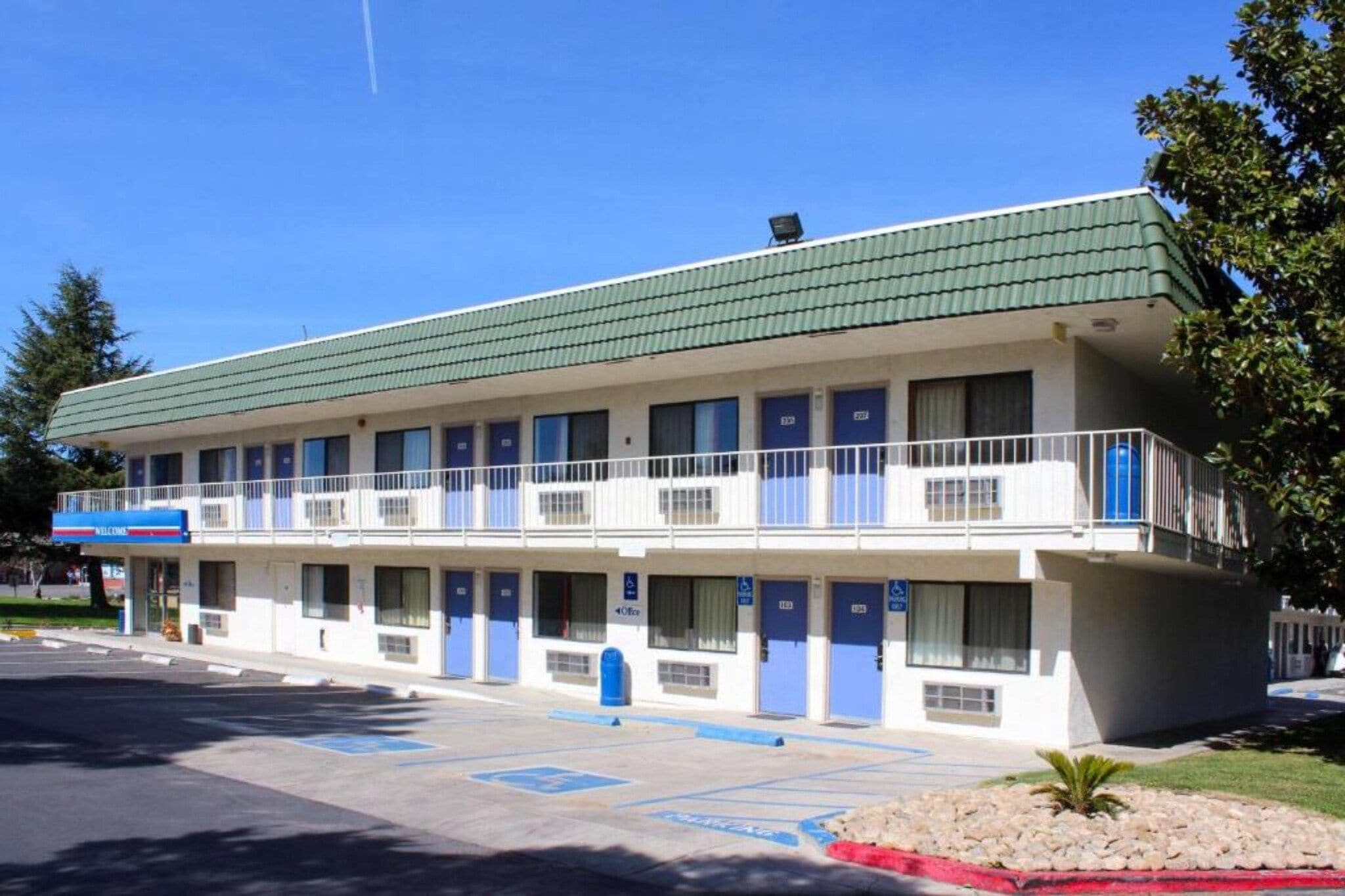 Un motel con techo verde, varias habitaciones y estacionamiento.