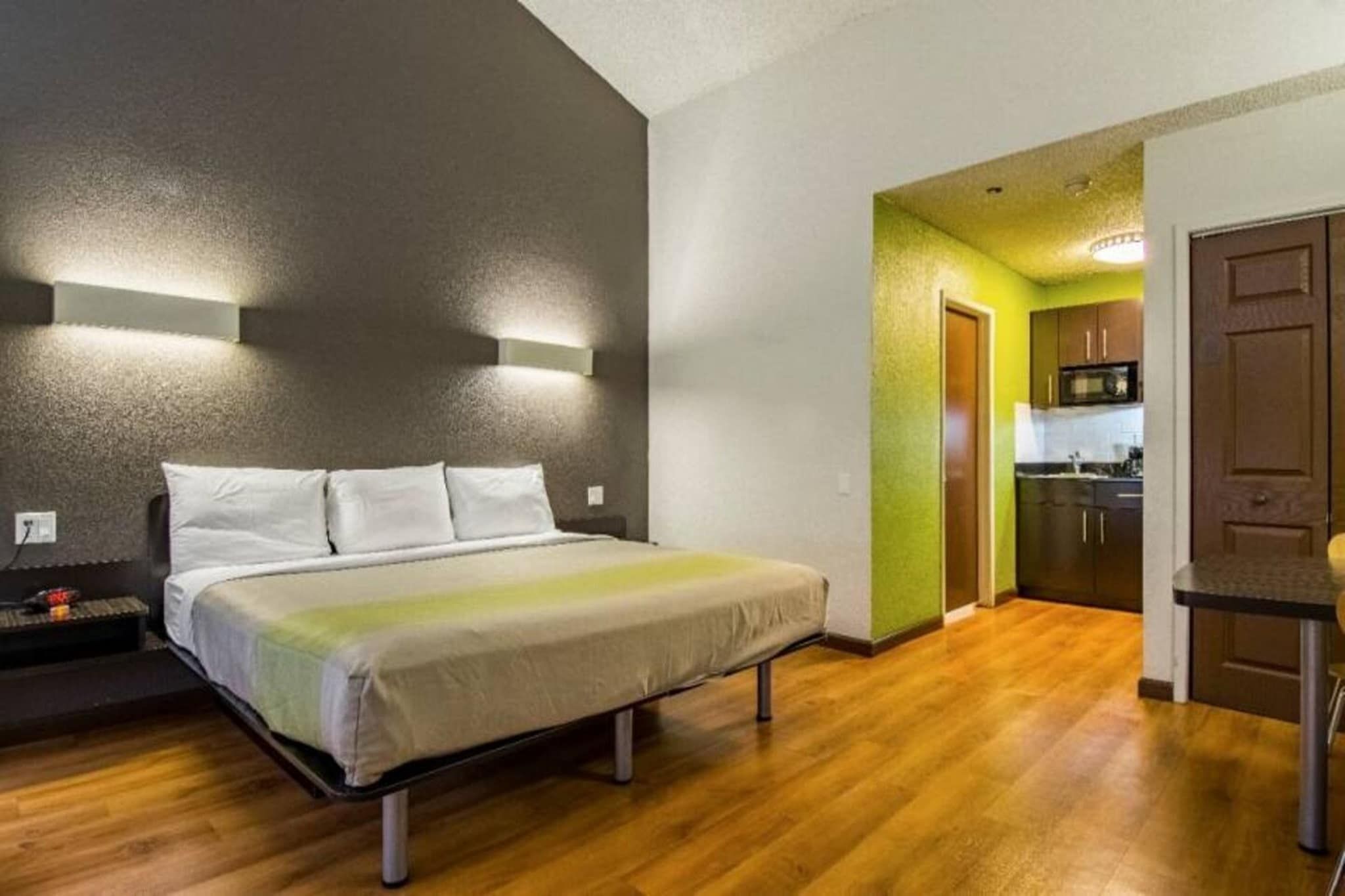 A bedroom with a bed, bedside tables, and a kitchenette in the adjacent room.