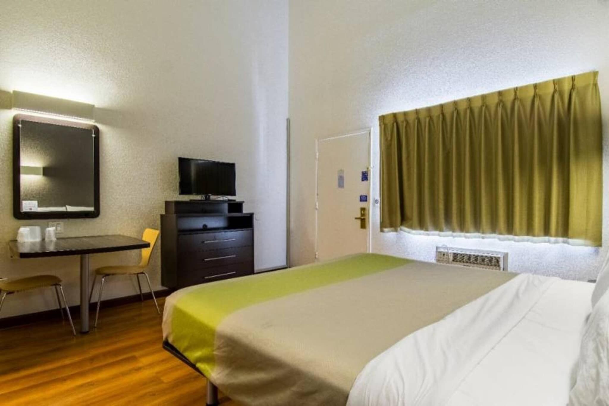A hotel room with a bed, a desk with a television, a chair, and a window with curtains.