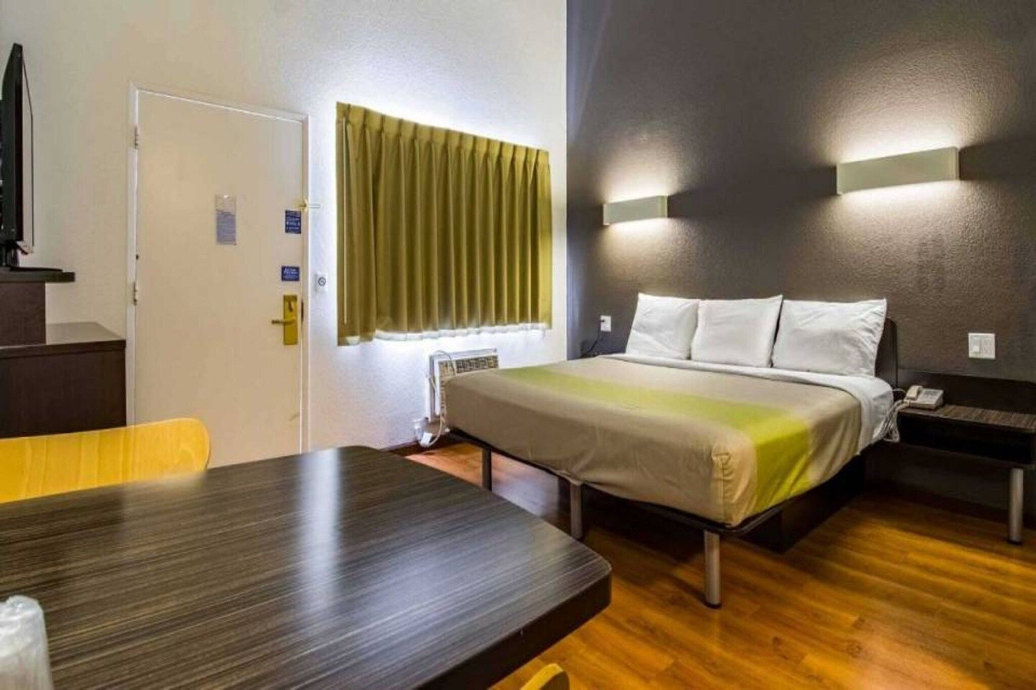 Hotellihuone, jossa on sänky, yöpöytä ja ikkuna, jossa on verhot.