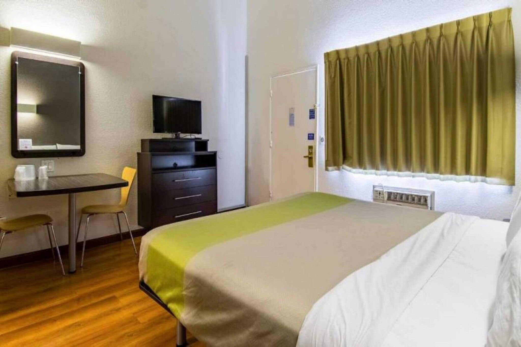 A hotel room with a bed, a desk, a chair, a television, and a window with curtains.