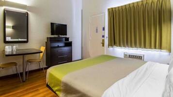 A hotel room with a bed, a desk, a chair, a television, and a window with curtains.