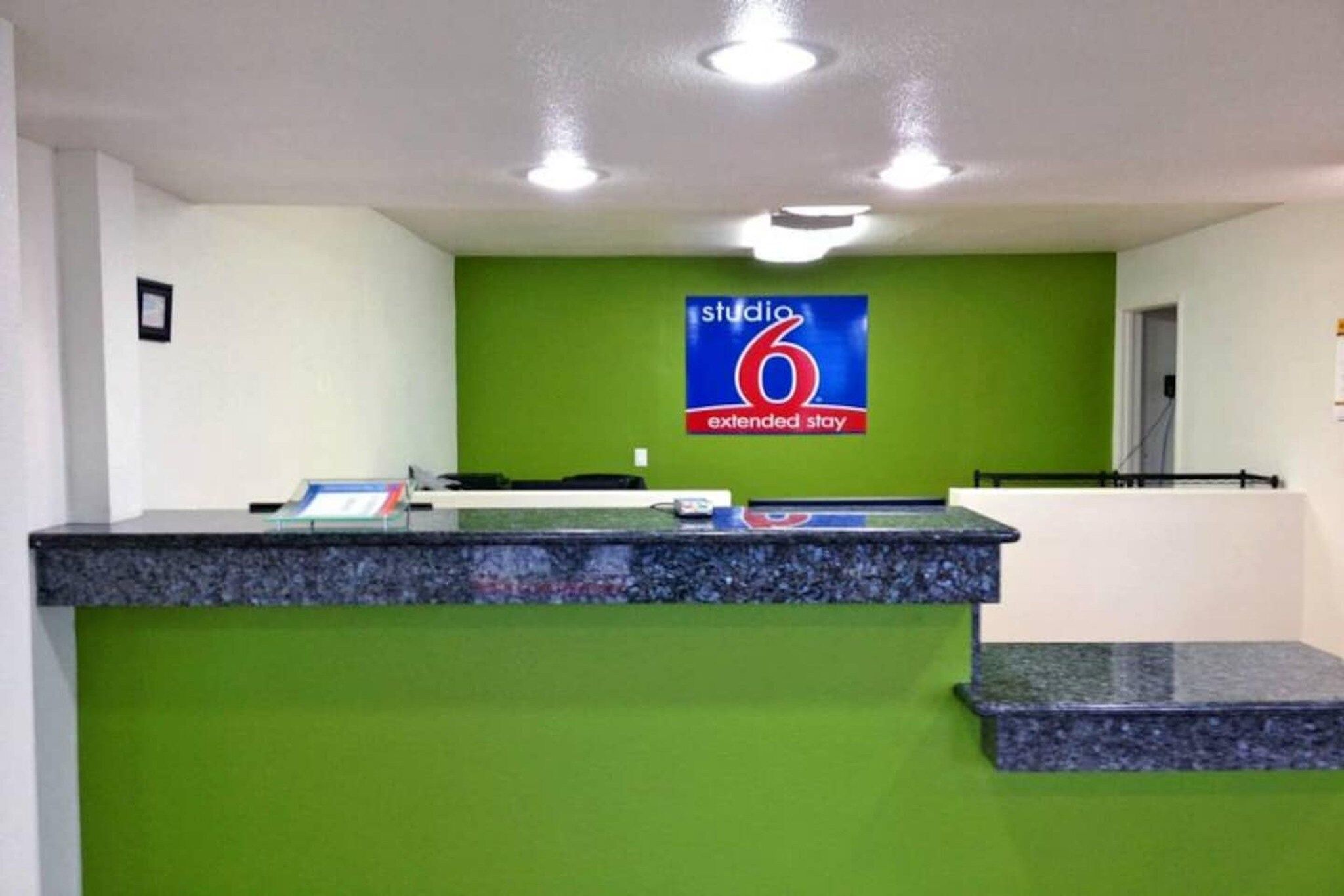 Una recepción con pared verde, un letrero que dice 'studio 6 extended stay' y un mostrador con una computadora y documentos.