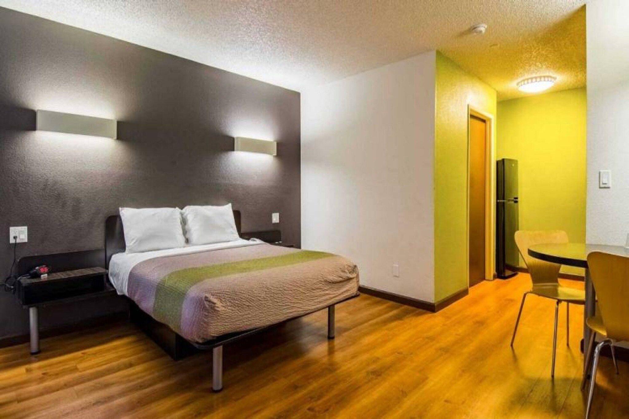 Hotellihuone, jossa on sänky, yöpöytä ja pieni työpöytä tuolilla.