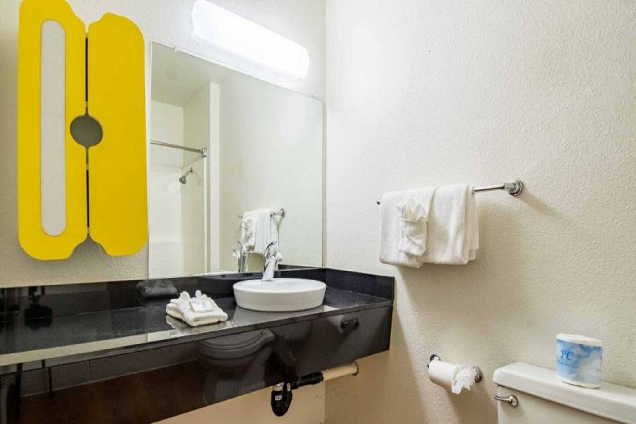 Een badkamer met een wastafel, spiegel, handdoekrek, toilet en toiletpapierhouder.