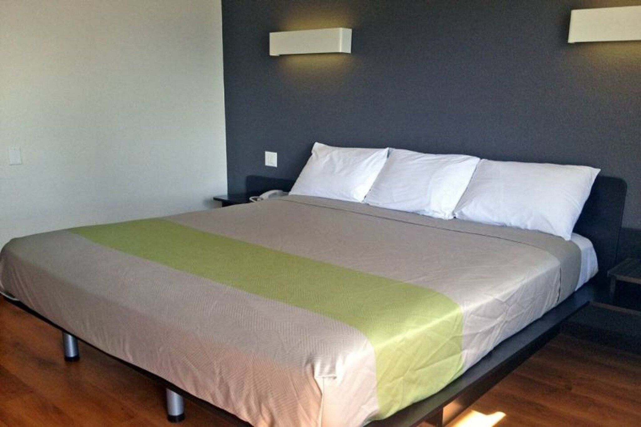 A bed with a beige and green bedspread, a dark headboard, and two wall-mounted light fixtures.