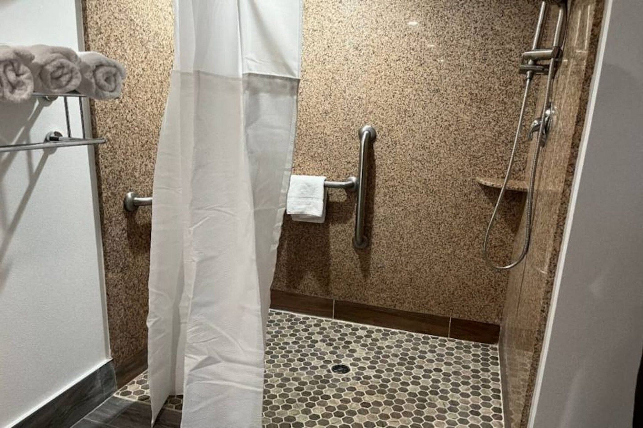 Un área de ducha con suelo de baldosas, un perchero y un panel de control de la ducha.