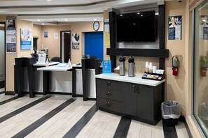 Zona de recepción con un mostrador, sillas, estación de café y un reloj en la pared.