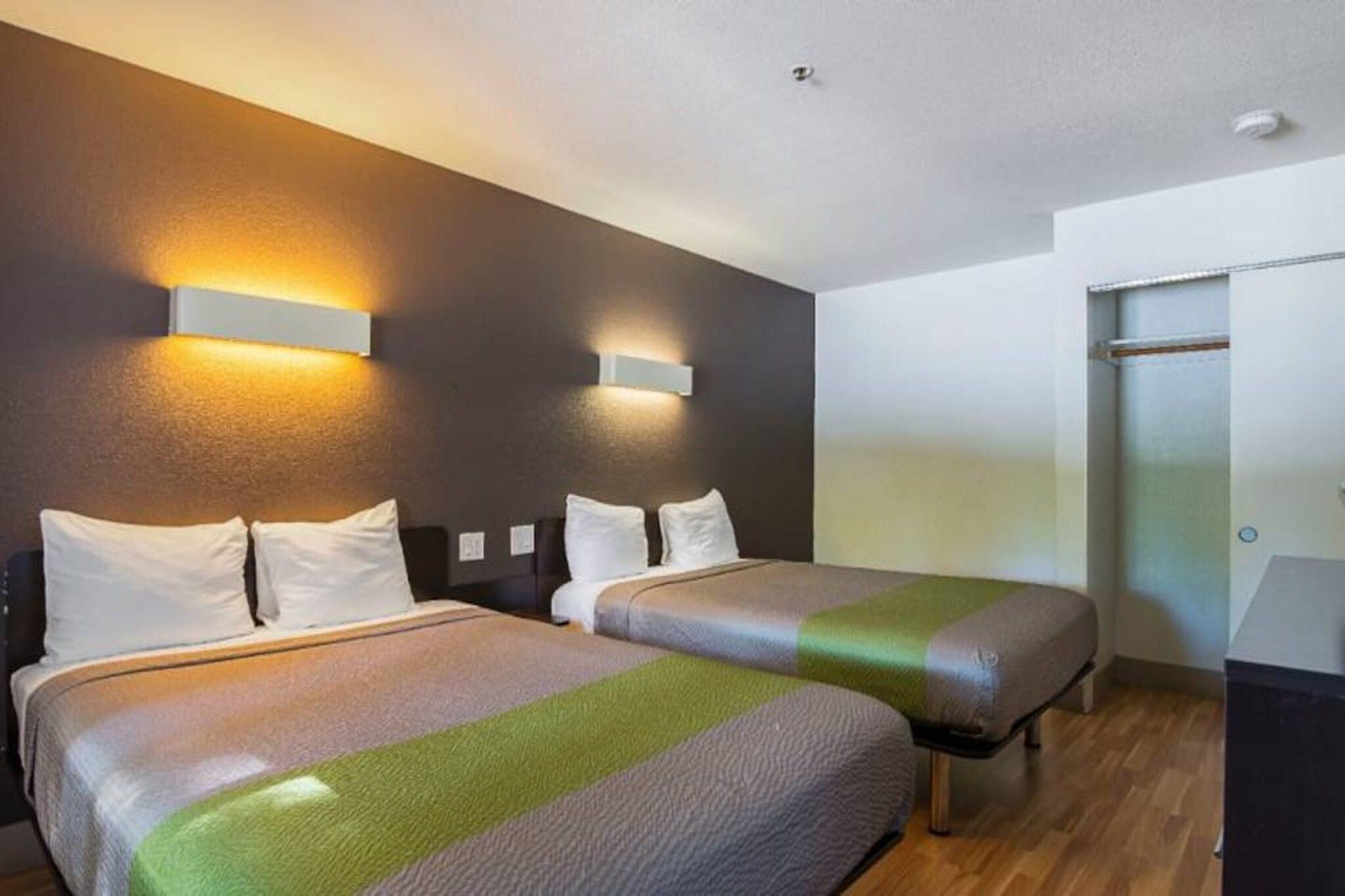 A hotel room with two beds, a wooden floor, and a sliding door closet.