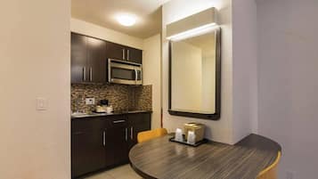 A compact kitchen with dark cabinets, a microwave, and a round dining table with chairs.