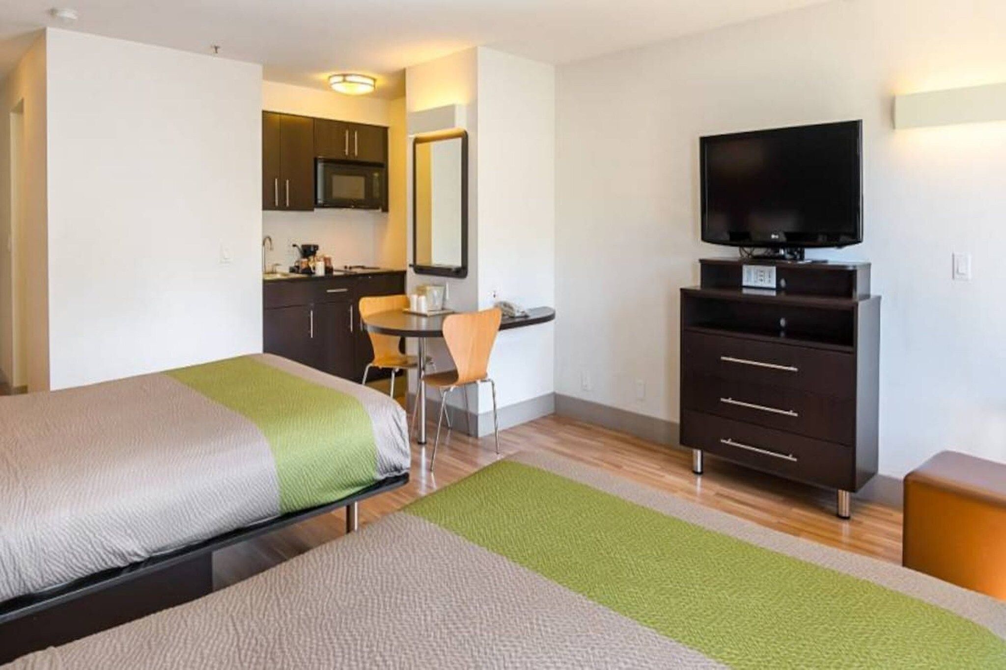A hotel room with a bed, a desk, a television, and a kitchenette.