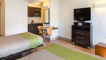 A hotel room with a bed, a desk, a television, and a kitchenette.
