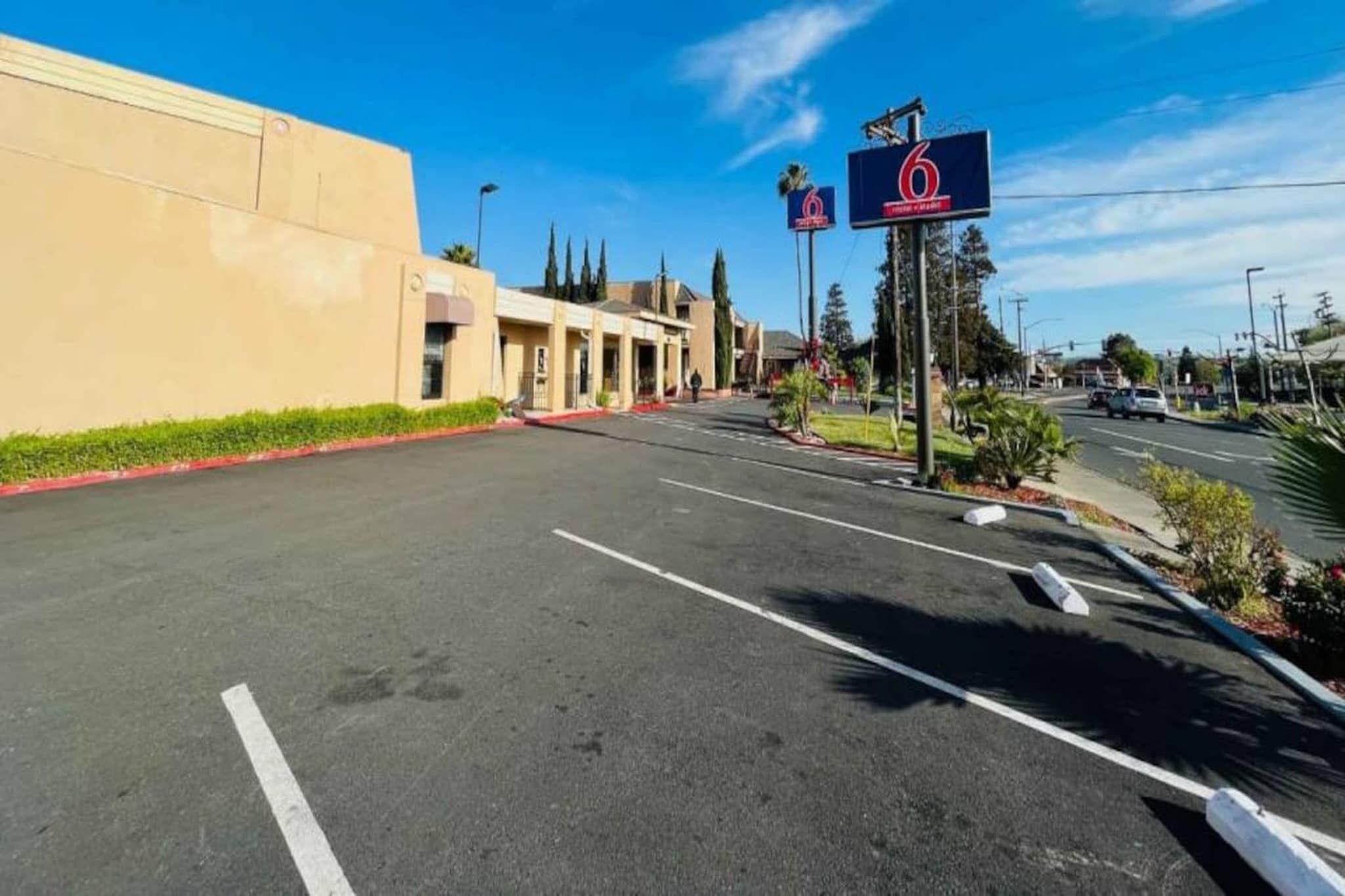 A parking lot with a building on the left and a road with a '6' sign on the right.