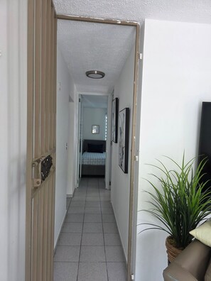 A narrow hallway with a bed at the end, a potted plant, and a door on the left. - Charming 3-bedroom House in Monte Vista Fajardo, Puerto Rico (Fajardo)