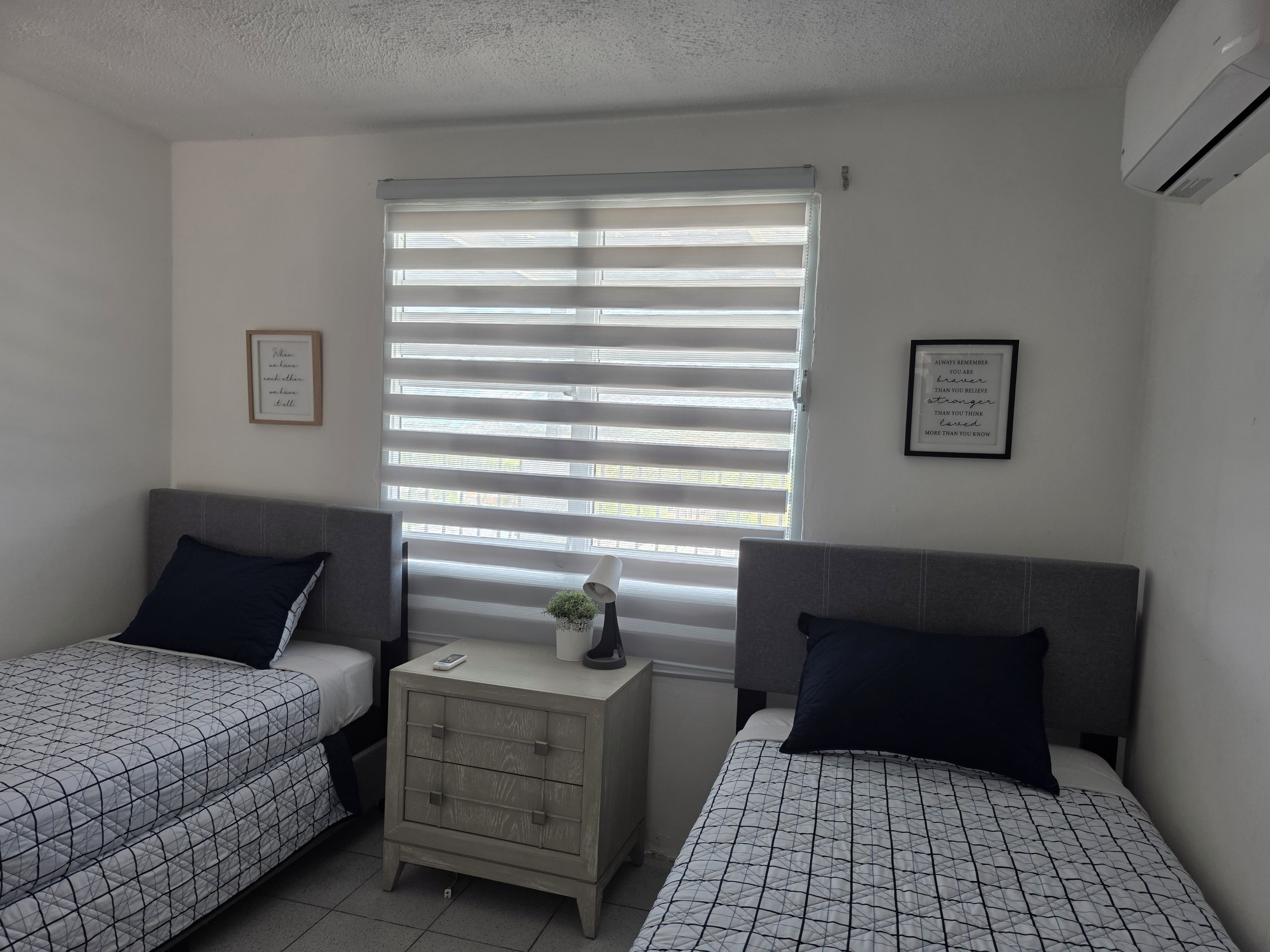 A bedroom with two beds, a bedside table, and a window with blinds.