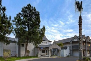 A modern building with a large tree and a palm tree in front. - Premium Queen Bed|Pool|Free Parking (Buttonwillow)