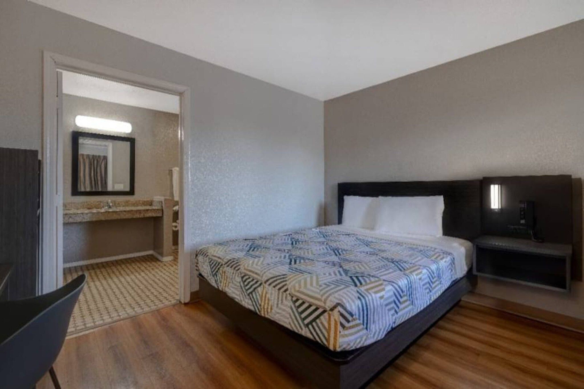 Habitación de hotel con cama, mesita de noche, espejo y puerta que da a un baño.