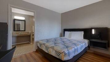 Habitación de hotel con cama, mesita de noche, espejo y puerta que da a un baño.
