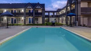 Una piscina con un patio circundante, una zona de estar cubierta y un edificio con varios balcones.