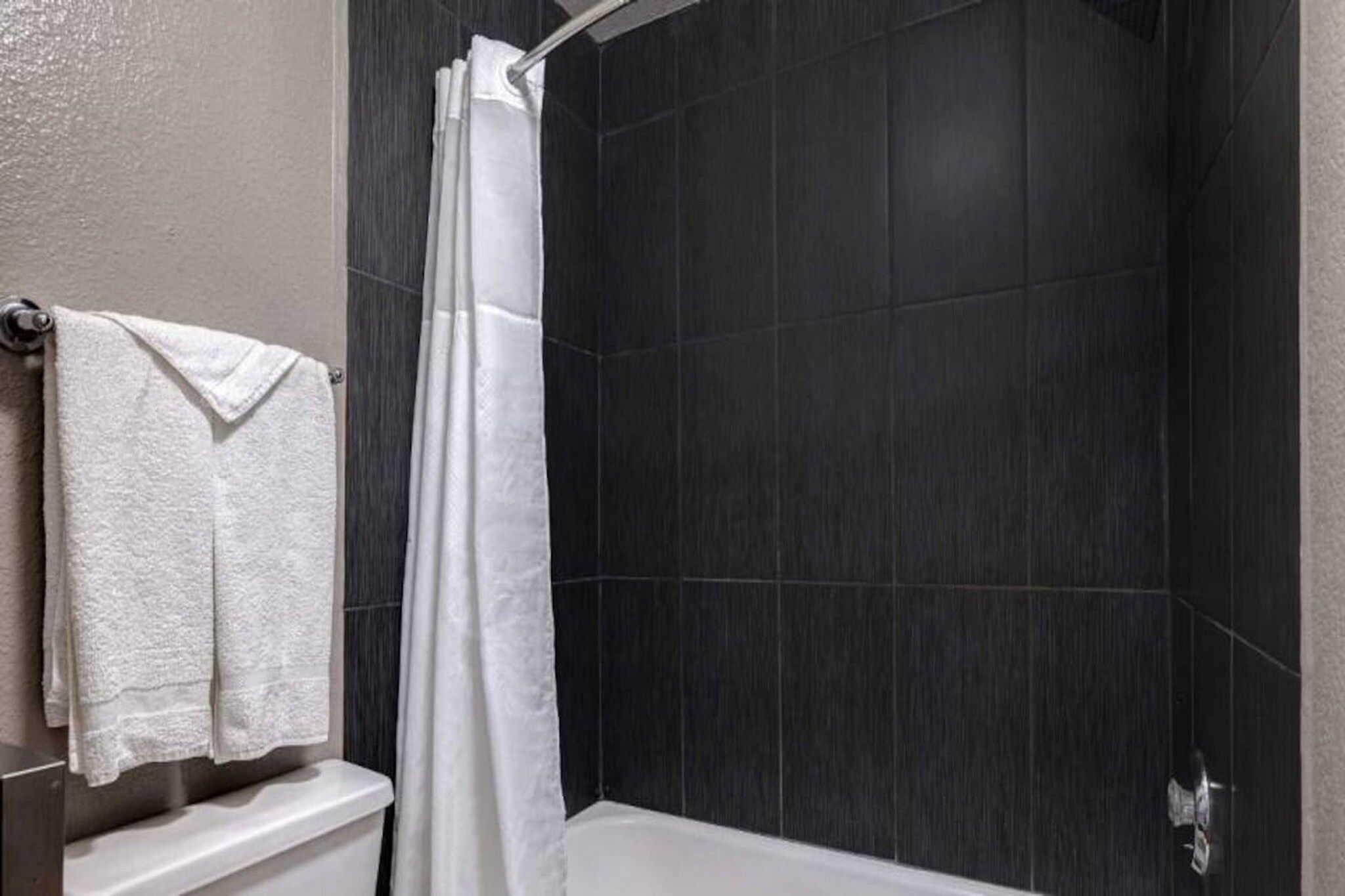 Ein Badezimmer mit Dusche, dunklen Fliesenwänden und einer weißen Toilette.
