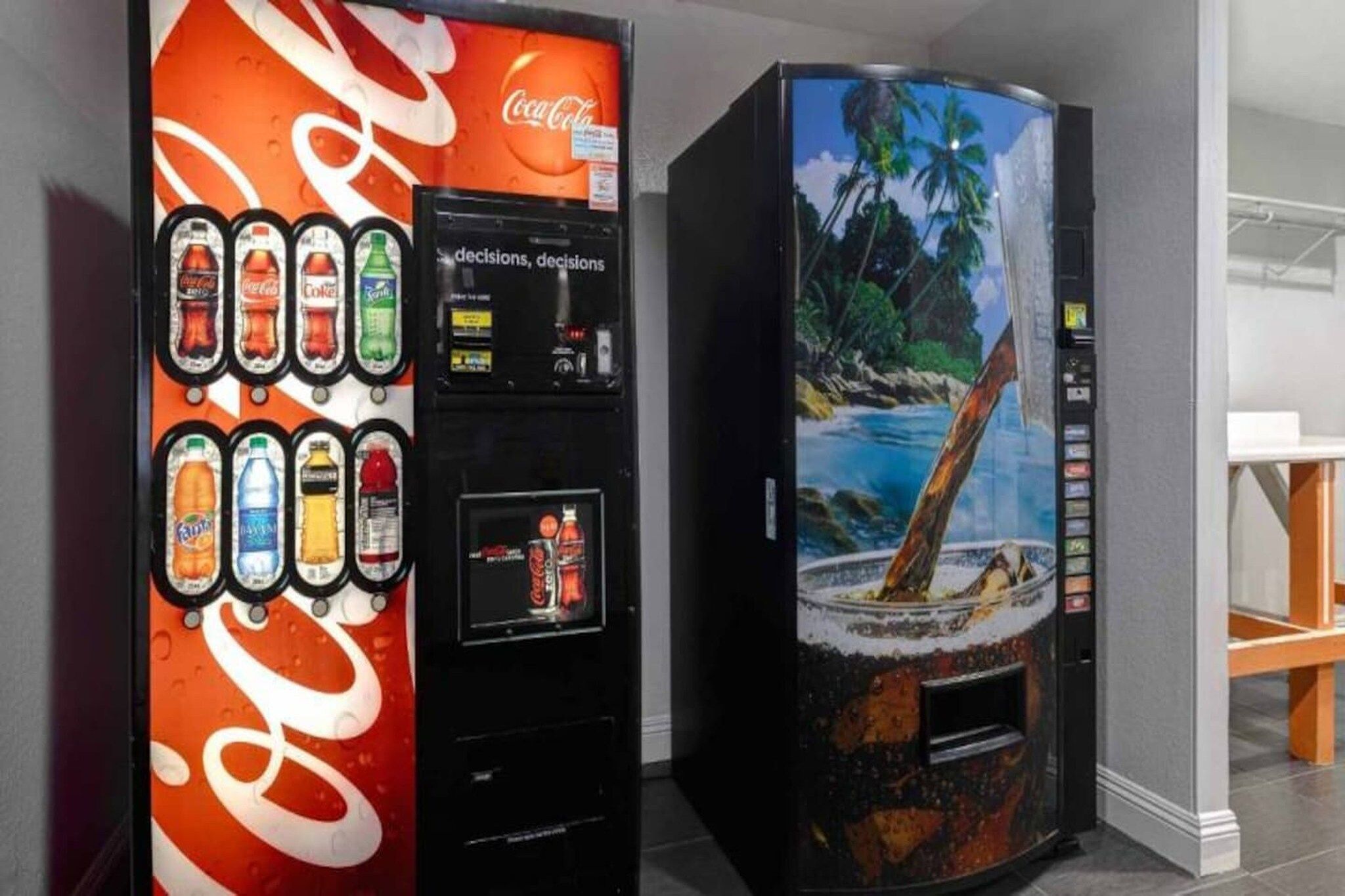 Dos máquinas expendedoras de bebidas, una con el logotipo de Coca-Cola y la otra con una imagen de una playa tropical.