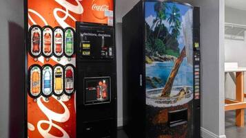 Dos máquinas expendedoras de bebidas, una con el logotipo de Coca-Cola y la otra con una imagen de una playa tropical.