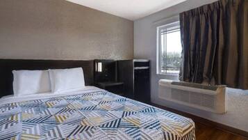 A hotel room with a bed, a heater, a window with curtains, and a wall-mounted air conditioning unit.