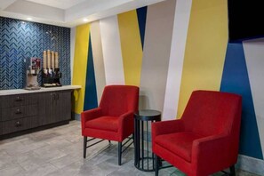 Un vestíbulo de hotel con dos sillones rojos, una cafetera y una recepción con un revestimiento de pared con patrón de espiga.