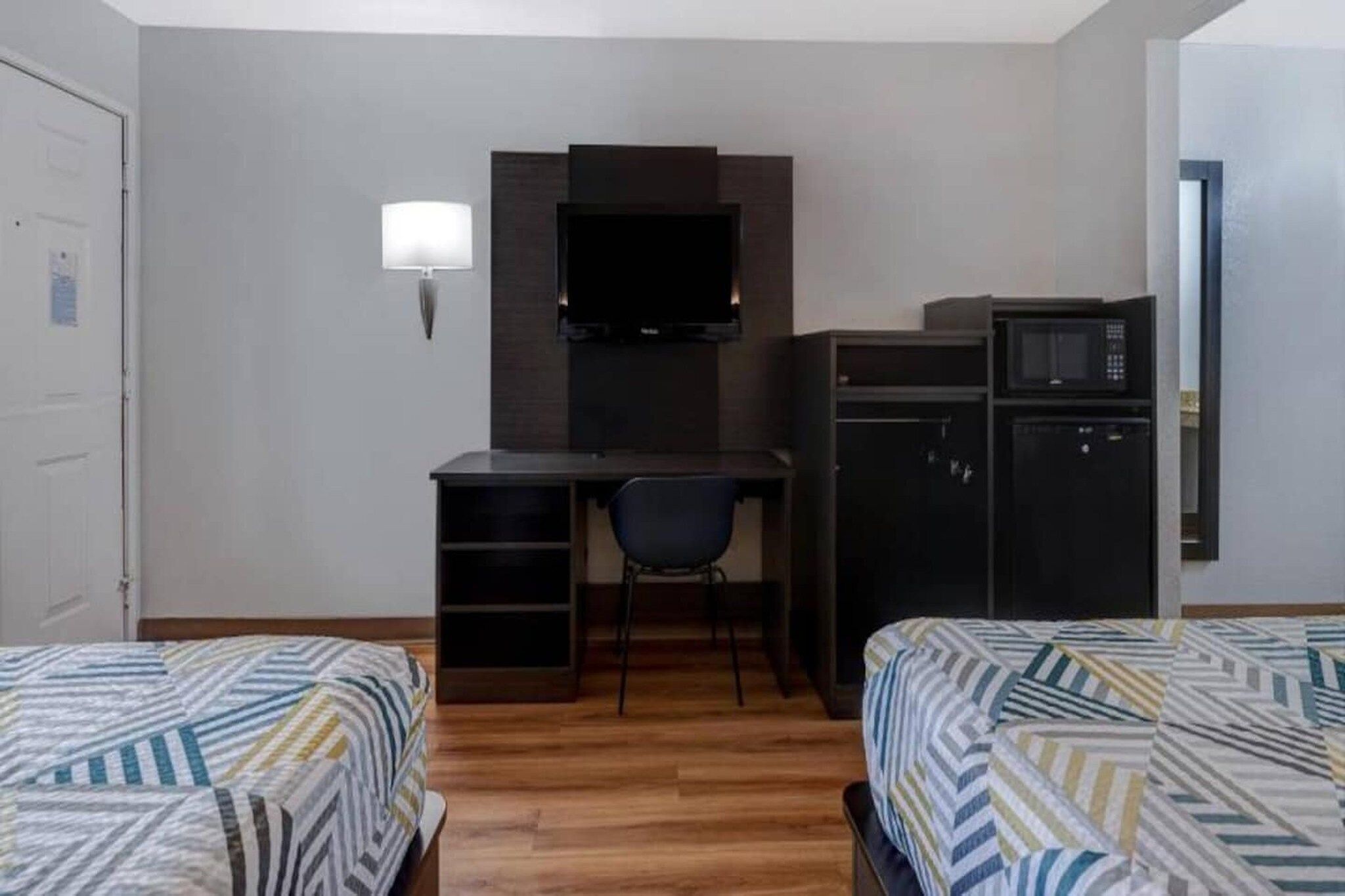 A hotel room with a bed, a desk with a chair, a television, and a microwave.