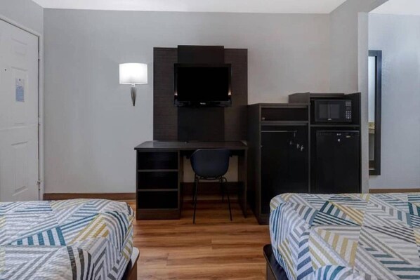 A hotel room with a bed, a desk with a chair, a television, and a microwave.