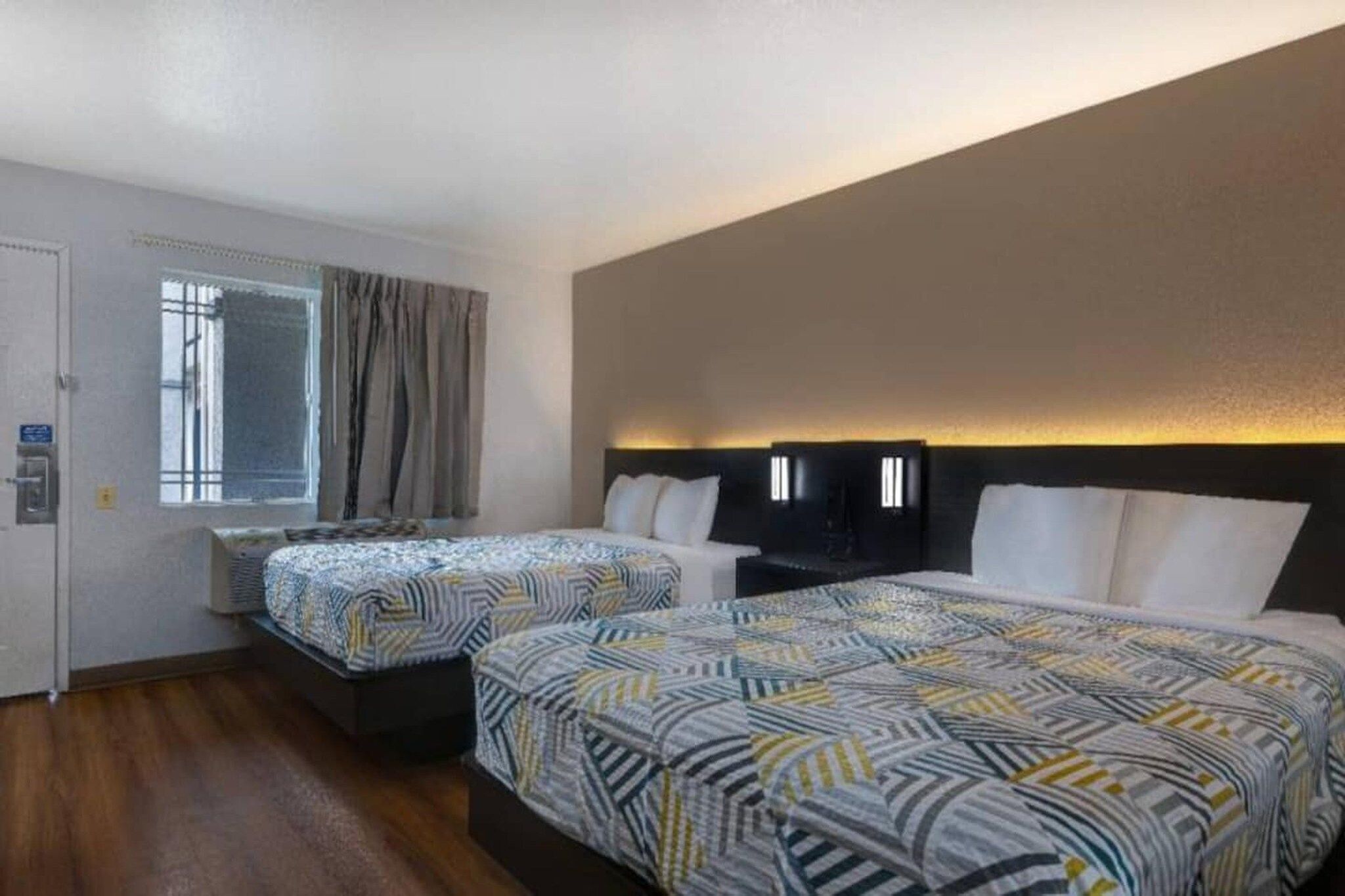 Une chambre d’hôtel avec deux lits, une fenêtre avec des rideaux et un luminaire fixé au mur.