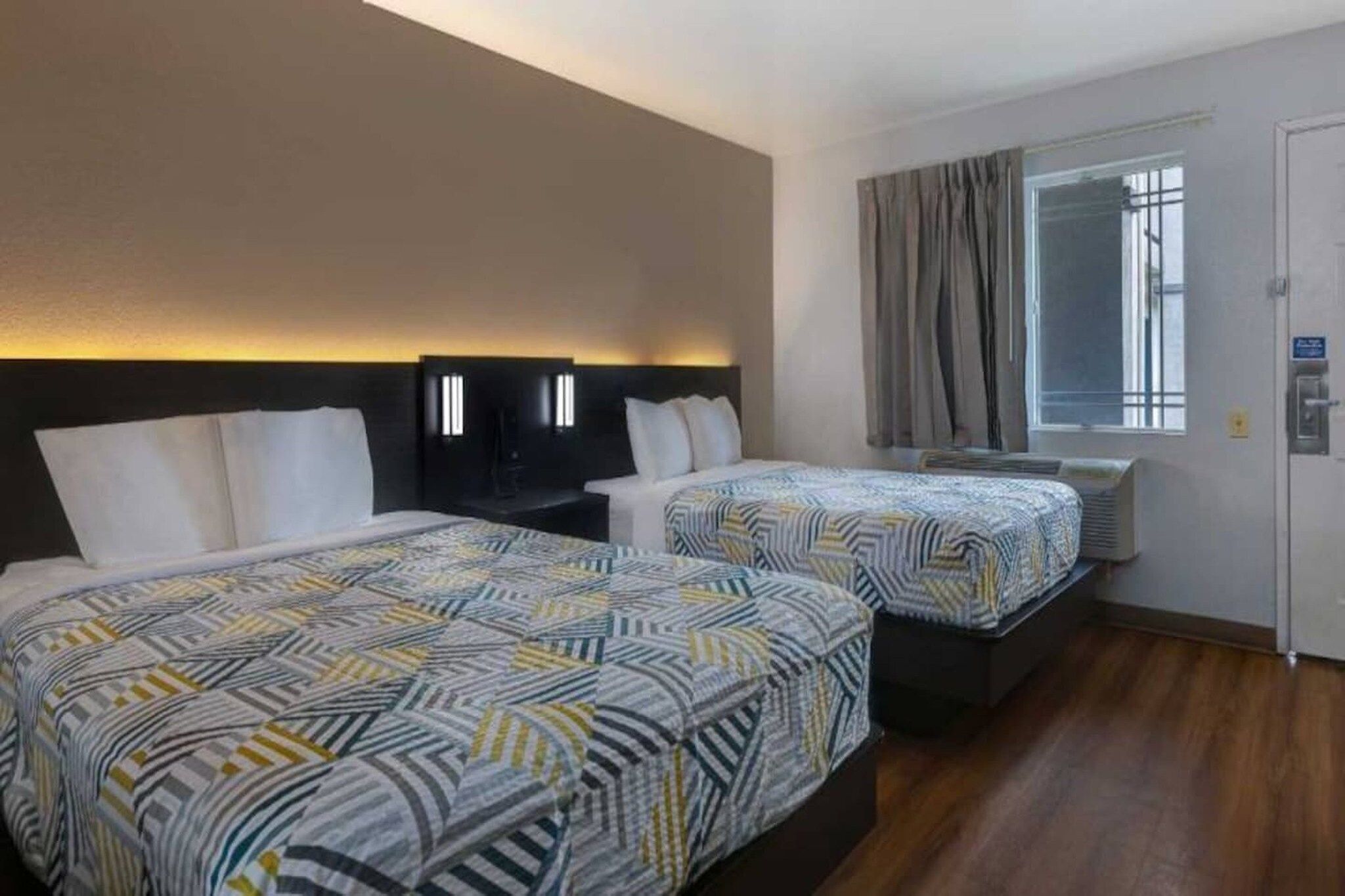 Una habitación de hotel con dos camas, una ventana con cortinas y un televisor montado en la pared.