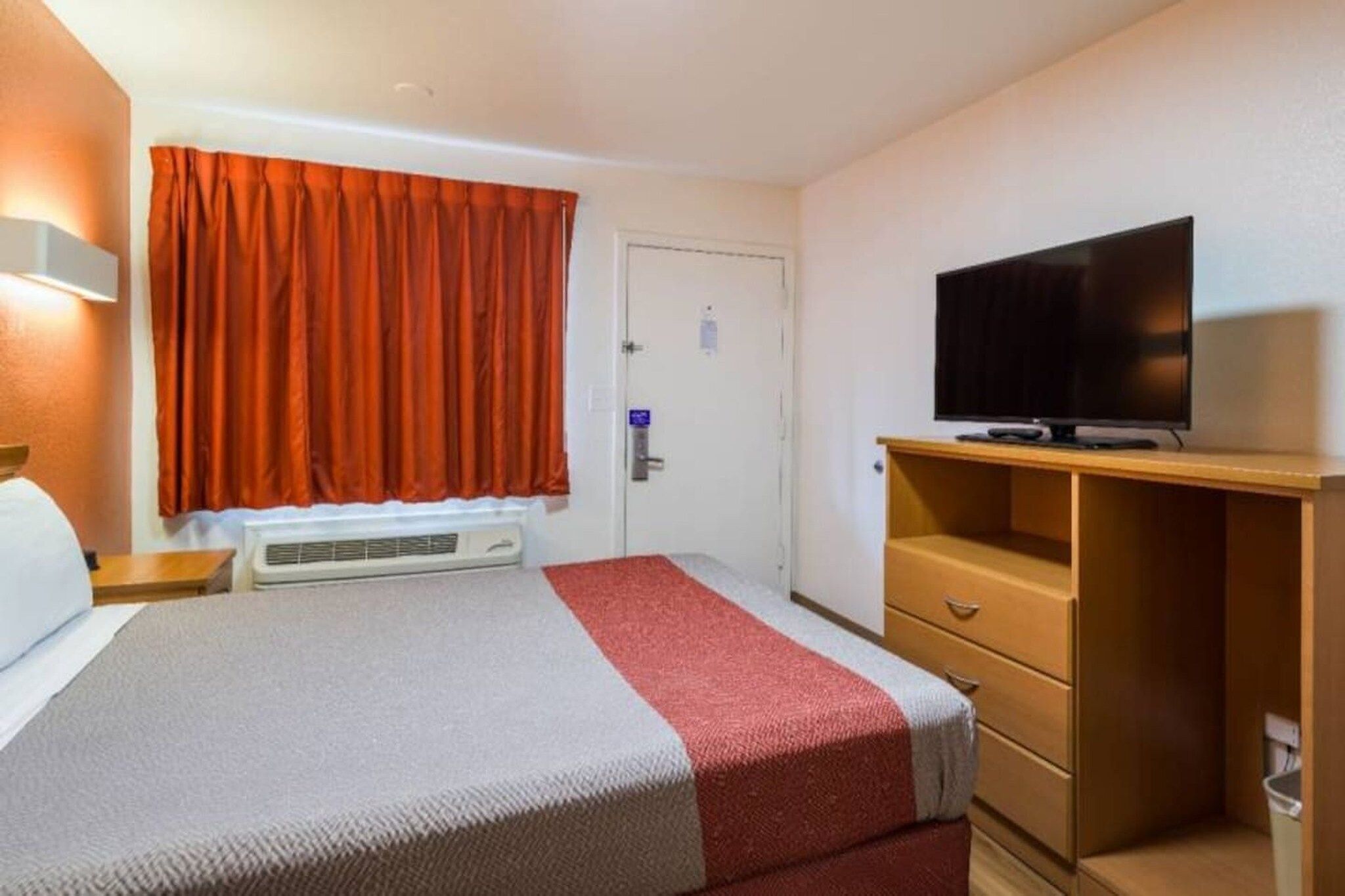 Una habitación de hotel con una cama, un televisor en un mueble, un armario y una puerta.