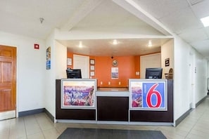 Ein Empfangsbereich mit einem Schreibtisch, zwei Computermonitoren, einem Schwarzesbretter und einem Poster an der Wand.