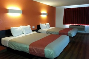 Ein Hotelzimmer mit zwei Betten, beide mit weißer Bettwäsche und roten Akzenten. An der Wand sind Lampen befestigt, und ein Fenster mit roten Vorhängen.