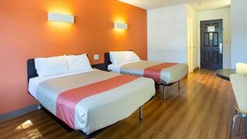 A hotel room with two beds, wooden flooring, and a door leading to another room.