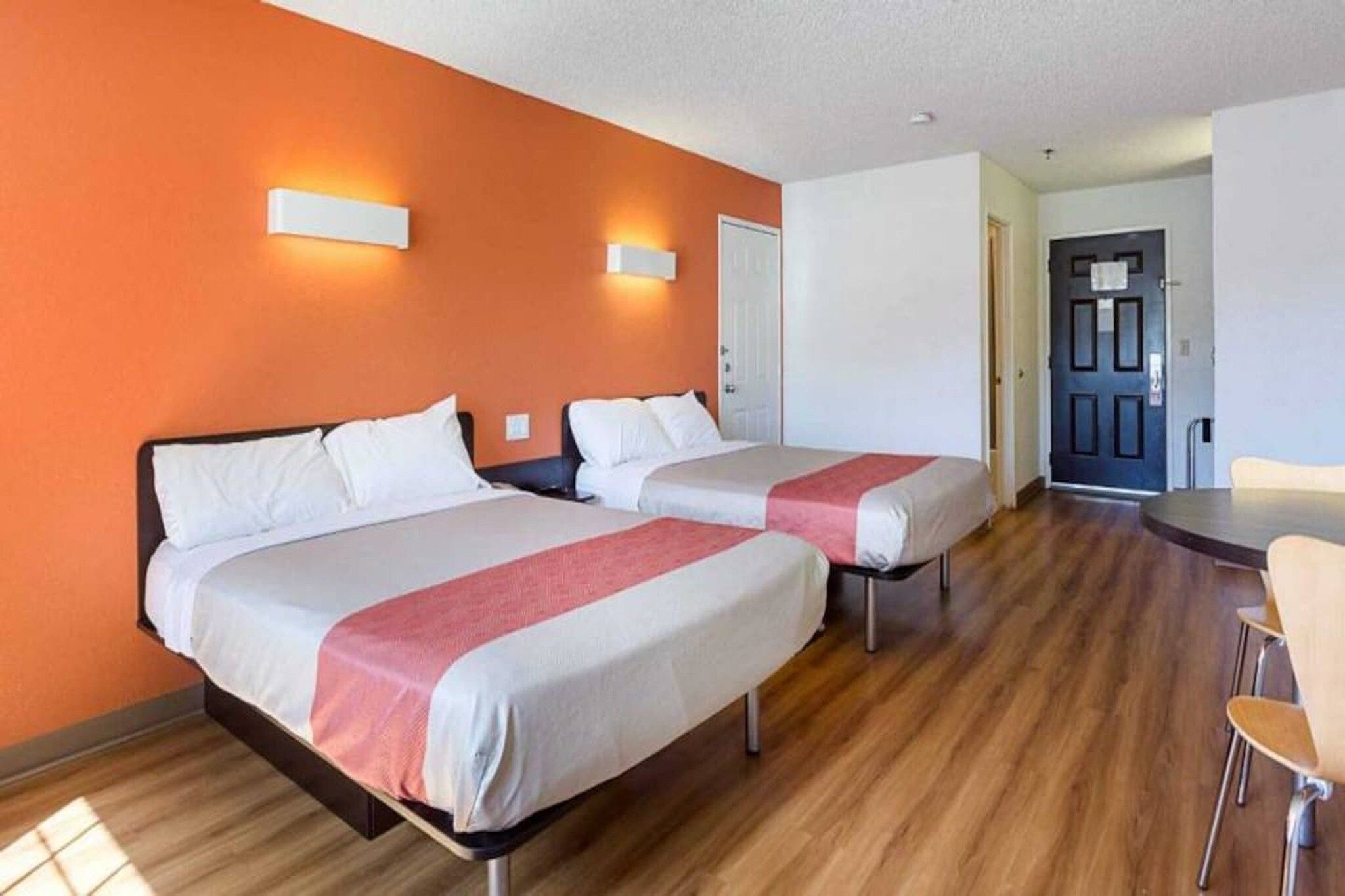 Quarto de hotel com duas camas, piso de madeira e porta que dá para uma sala de jantar.