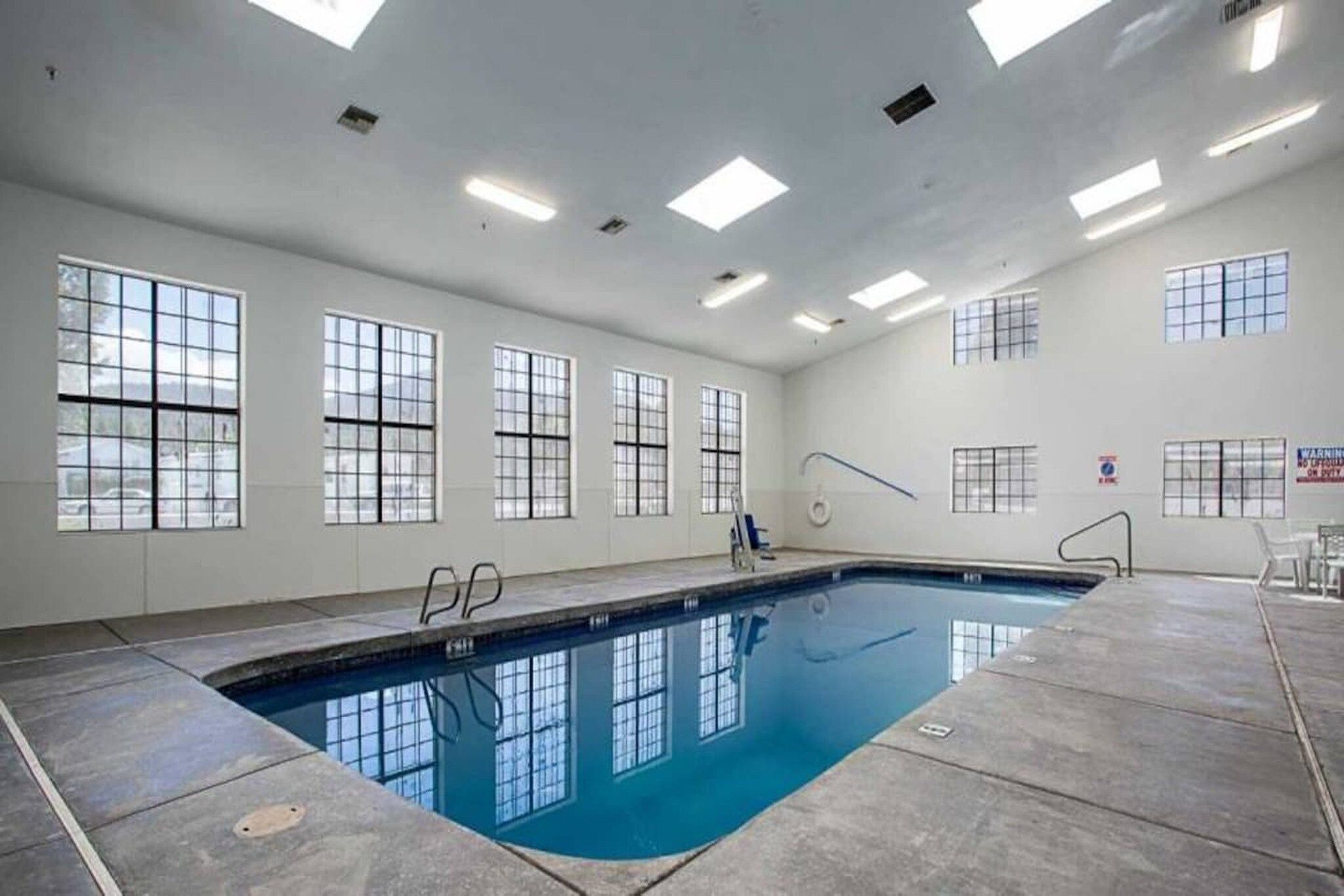 Ein Schwimmbecken mit klarem Wasser, umgeben von einer gefliesten Terrasse, und großen Fenstern an den Wänden.