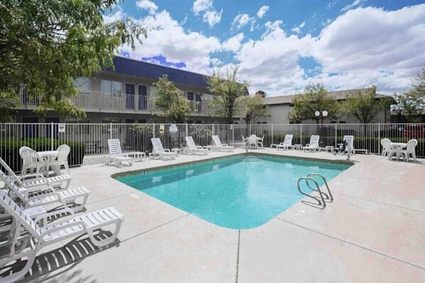 A rectangular outdoor swimming pool with a white fence surrounding it, and several white lounge chairs along the edge.