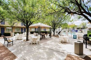 An outdoor patio area with tables and chairs, surrounded by trees and a building with a blue door. - 1 Queen Bed | Non-Smoking (Holbrook)