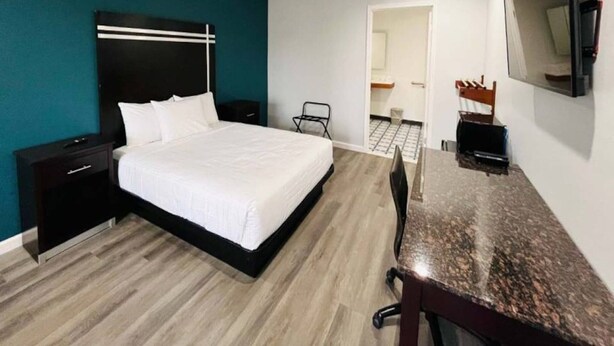 Habitación de hotel con cama, escritorio, silla, televisión y puerta que da a un baño.