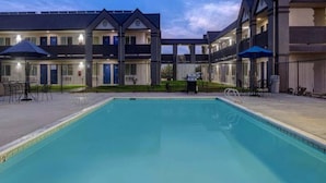 Una piscina con un patio circundante, una zona de estar cubierta y un edificio con varios balcones.