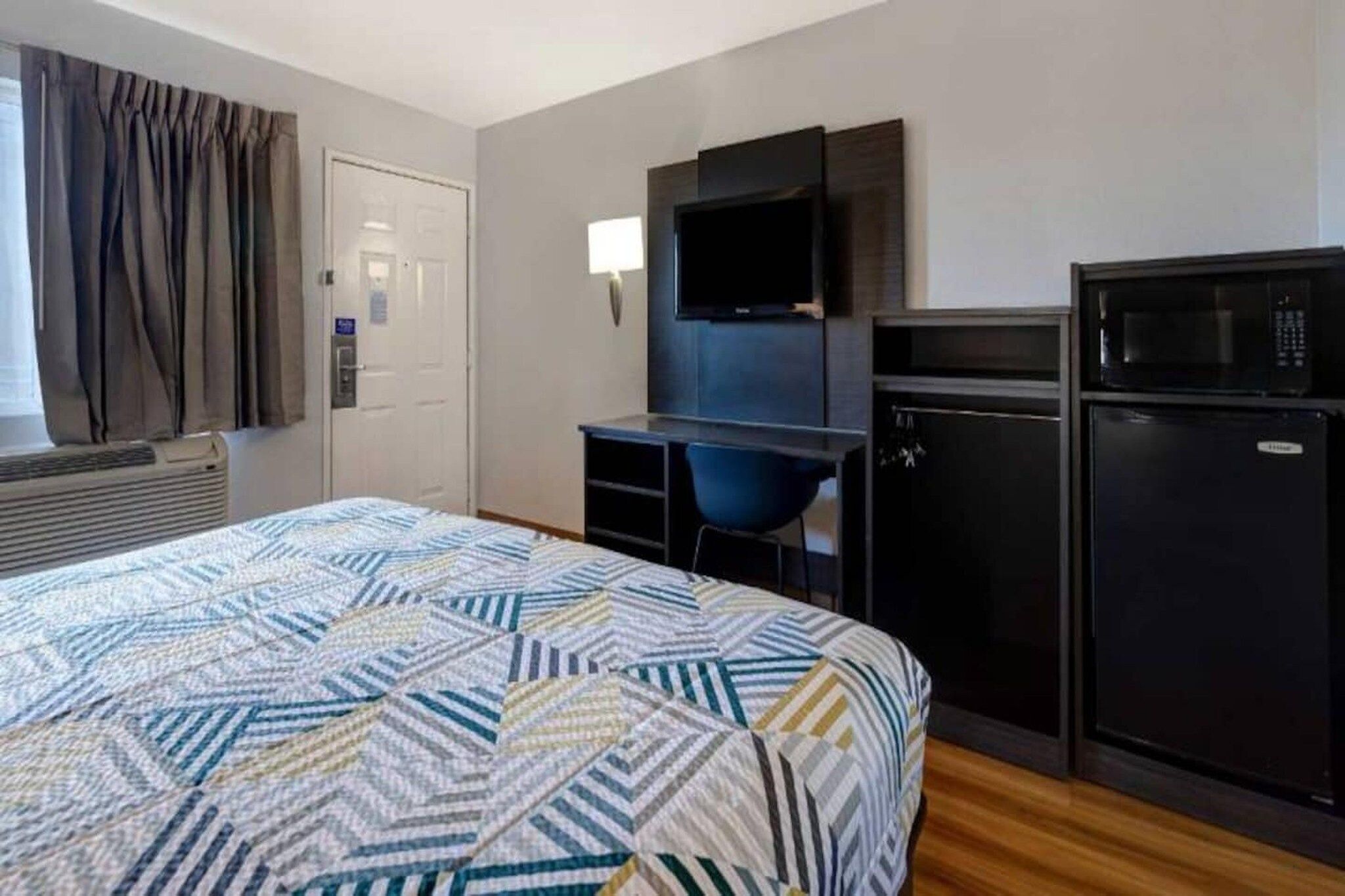 Une chambre d’hôtel équipée d’un lit, d’un bureau, d’une chaise, d’une télévision, d’un four à micro-ondes et d’un réfrigérateur.
